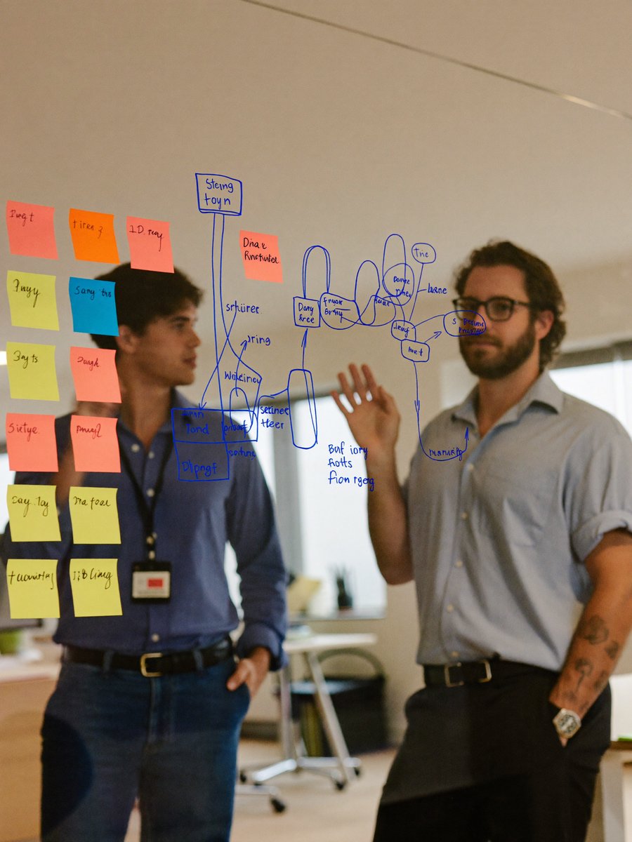 Two consultants working through a flow diagram and sticky notes on a glass wall